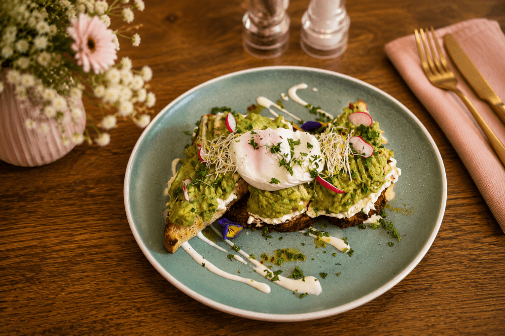 Avocado-Stulle mit pochiertem Ei, frischen Kräutern und Radieschen auf rustikalem Brot bei Frau Miller.