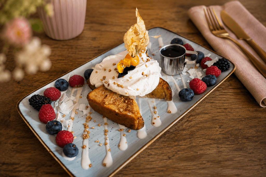 Französischer Toast mit cremigem Topping, frischen Beeren und Sirup auf einer stilvoll angerichteten Platte im Frühstückslokal Frau Miller.